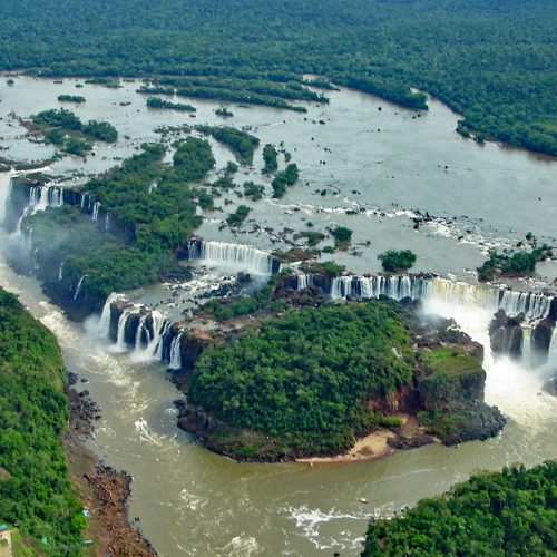 The wide cascades of Iguazu Falls surrounded by rainforest The wide cascades of Iguazu Falls surrounded by rainforest